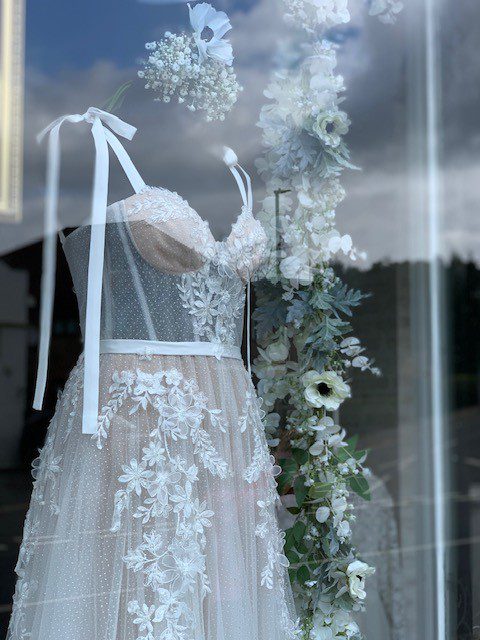 Hand‑styled international window display with faux floral installations for May & Grace boutique in Haslemere, Surrey.