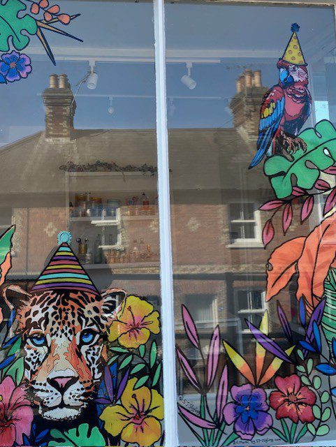 Hand‑painted window mural artwork of leopard and parrot with bold tropical foliage for Party Arty, Haslemere Surrey.