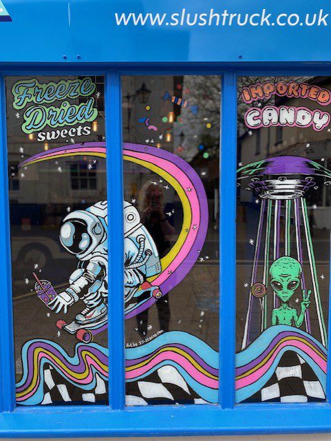Hand‑painted window mural artwork featuring astronaut with lollipop, green alien and colourful candy graphics for Slush Truck sweets shop in Alton Hampshire 