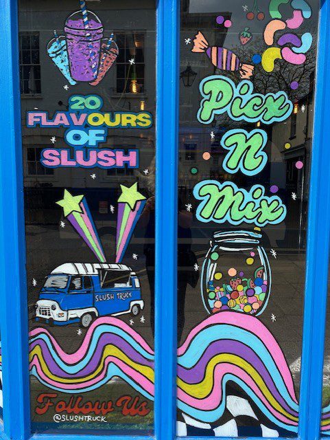 Hand‑painted window mural artwork of slush drink, pick‑and‑mix sweets and Slush shop Truck candy van with bold rainbow graphics in Alton Hampshire 