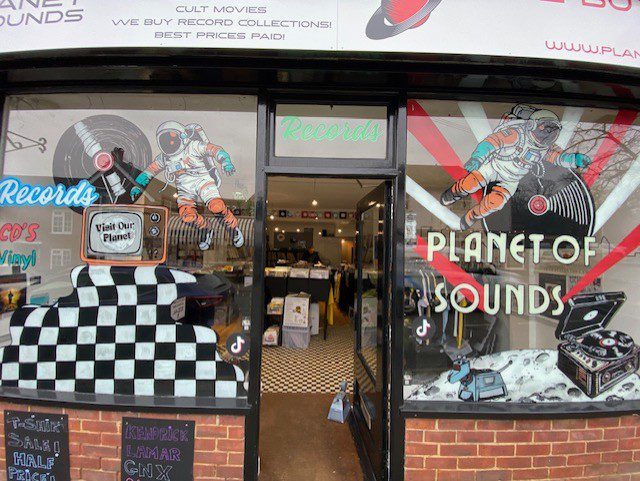 Hand‑painted window mural artwork featuring astronauts, vinyl records and retro music graphics across the Planet of Sounds shopfront in Haslemere, Surrey.