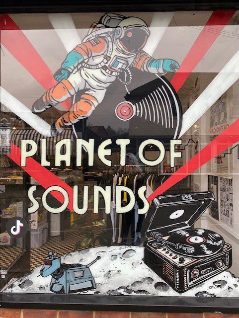 Hand‑painted window mural artwork featuring two astronauts holding vinyl records for Planet of Sounds music shop in Haslemere, Surrey.