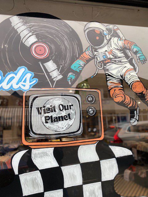 Hand‑painted window mural artwork featuring astronaut, retro TV and vinyl record with “Visit Our Planet” for Planet of Sounds in Haslemere, Surrey.